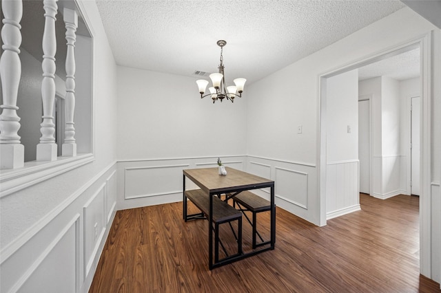 dining space with dark hardwood / wood-style floors, a textured ceiling, and an inviting chandelier