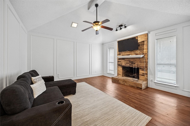 living room featuring a fireplace, a wealth of natural light, wood-type flooring, a textured ceiling, and vaulted ceiling