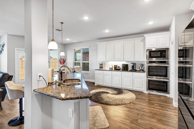 kitchen featuring sink, white cabinets, a kitchen bar, and dark stone countertops