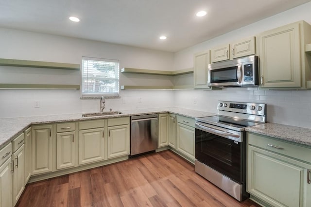 kitchen with sink, stainless steel appliances, light wood-type flooring, and light stone countertops