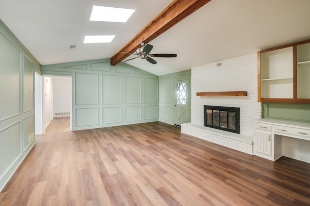 unfurnished living room featuring ceiling fan, light hardwood / wood-style flooring, a brick fireplace, and vaulted ceiling with skylight