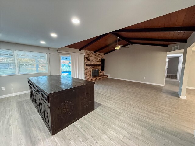 kitchen with visible vents, light wood-style flooring, dark countertops, a brick fireplace, and vaulted ceiling with beams