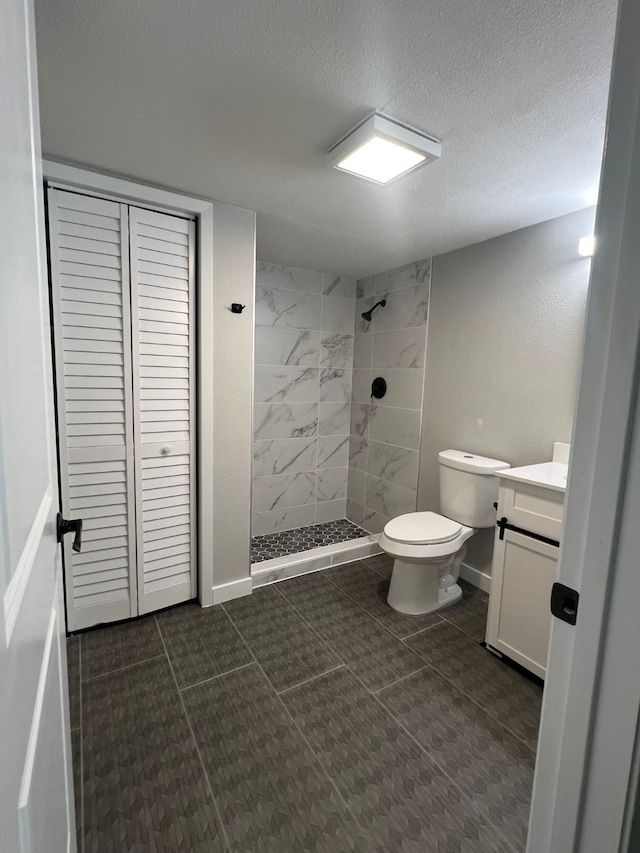 full bathroom with a textured ceiling, toilet, vanity, and a tile shower