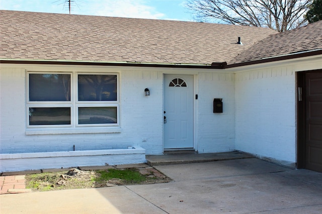 view of exterior entry featuring a garage, brick siding, and a shingled roof