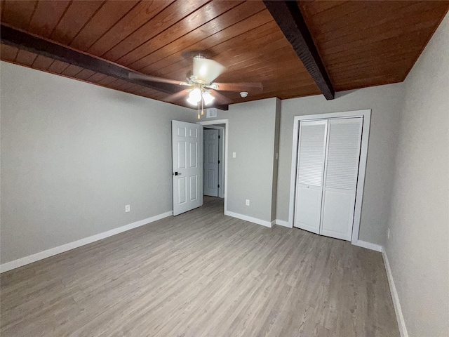 unfurnished bedroom with beamed ceiling, wood finished floors, a closet, baseboards, and wood ceiling