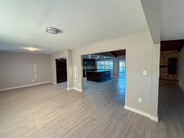 unfurnished living room with light wood-style floors, baseboards, and a textured ceiling