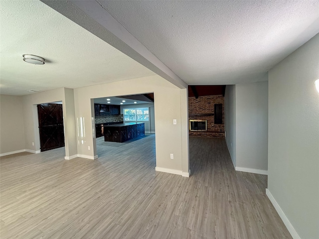 unfurnished living room with wood finished floors, a fireplace, baseboards, and a textured ceiling