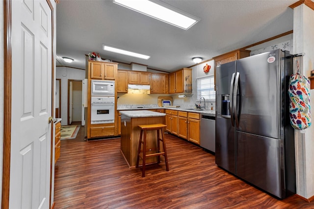 kitchen with appliances with stainless steel finishes, a center island, dark hardwood / wood-style flooring, a kitchen bar, and lofted ceiling