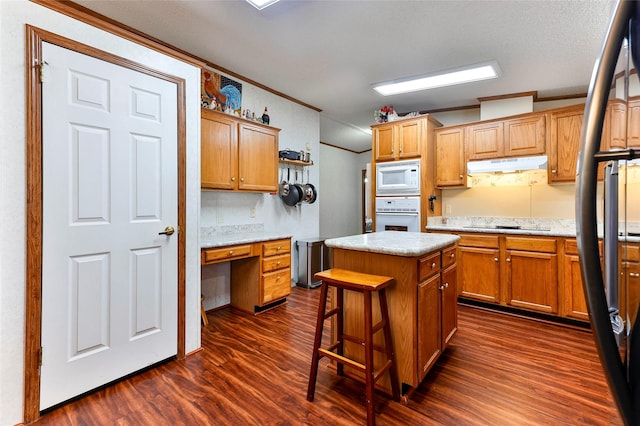 kitchen with white appliances, dark wood-type flooring, a center island, a kitchen bar, and crown molding