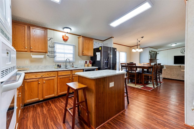 kitchen with black fridge with ice dispenser, a center island, decorative light fixtures, a kitchen bar, and sink