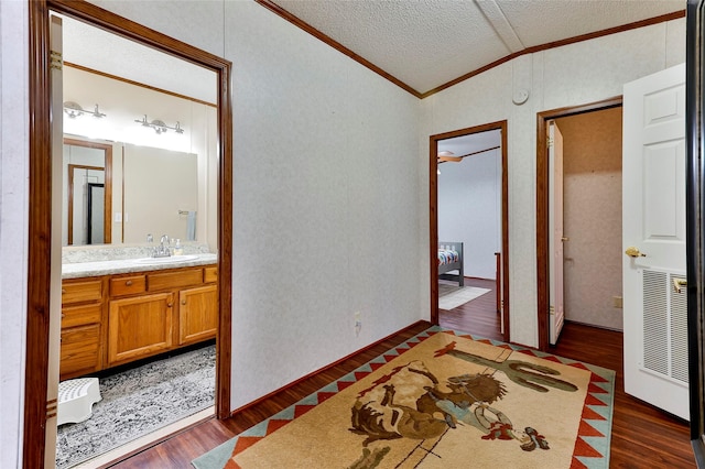 bedroom with ensuite bath, ornamental molding, a textured ceiling, dark hardwood / wood-style floors, and sink