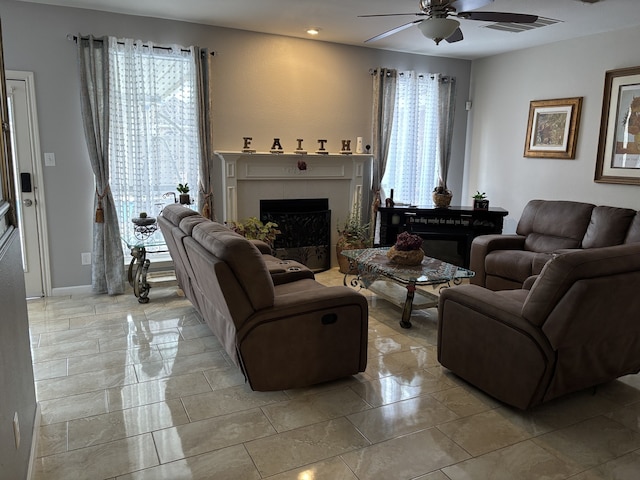 living room with ceiling fan, a tile fireplace, and light tile patterned flooring