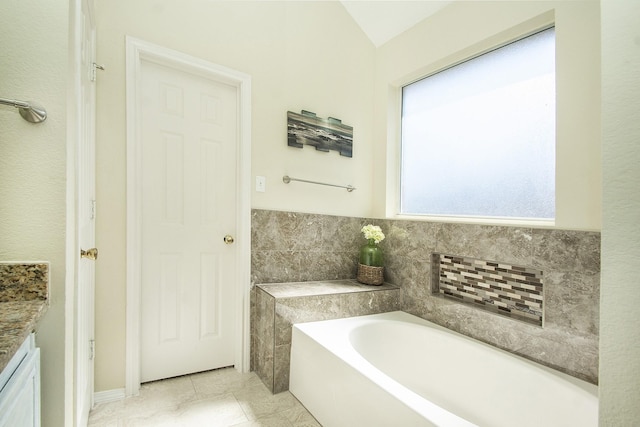 bathroom with a tub, vanity, lofted ceiling, and tile patterned flooring