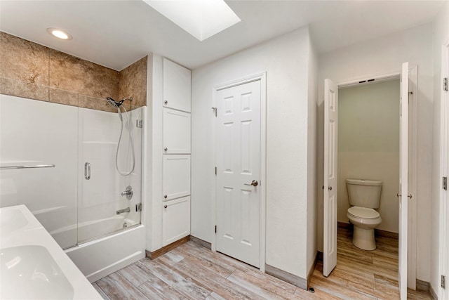 bathroom with wood-type flooring, combined bath / shower with glass door, toilet, double sink, and a skylight