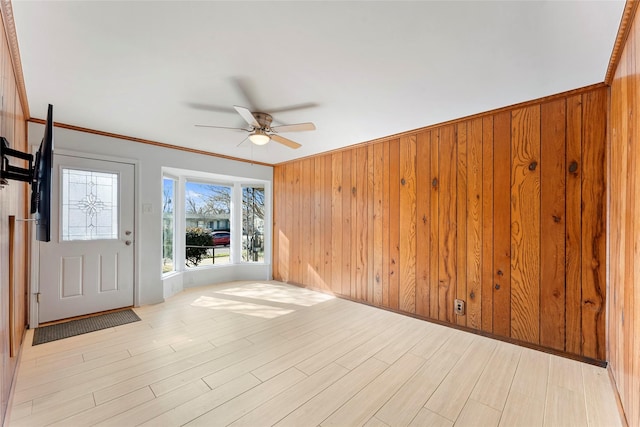 foyer entrance featuring ornamental molding, ceiling fan, light hardwood / wood-style floors, and wooden walls