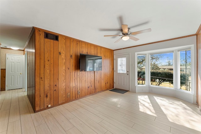 unfurnished living room featuring ceiling fan, wood walls, ornamental molding, and light wood-type flooring