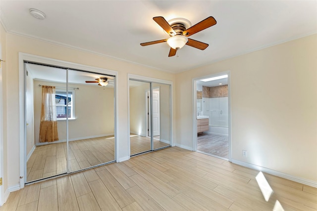 unfurnished bedroom featuring ceiling fan, ensuite bathroom, and two closets