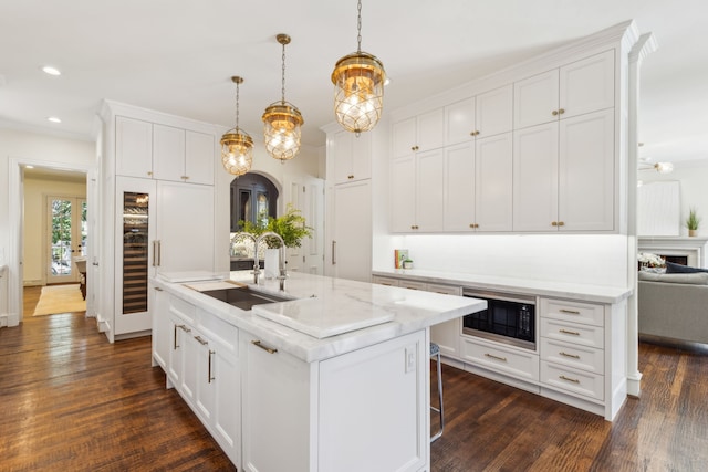 kitchen featuring a center island with sink, black microwave, sink, white cabinetry, and decorative light fixtures