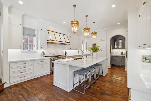 kitchen with a large island with sink, high end range, white cabinetry, and hanging light fixtures