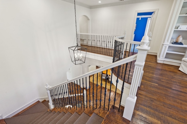 staircase with an inviting chandelier, crown molding, and wood-type flooring