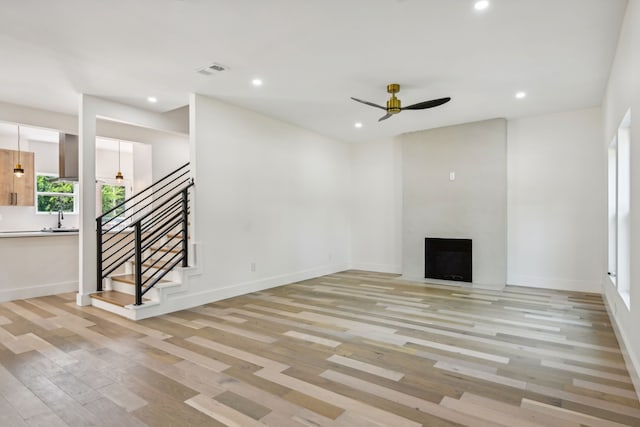 unfurnished living room with a large fireplace, ceiling fan, light hardwood / wood-style floors, and sink