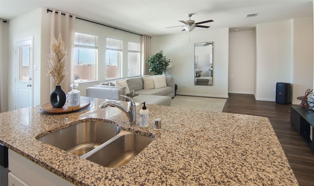 kitchen featuring ceiling fan, sink, dark wood-type flooring, and light stone counters