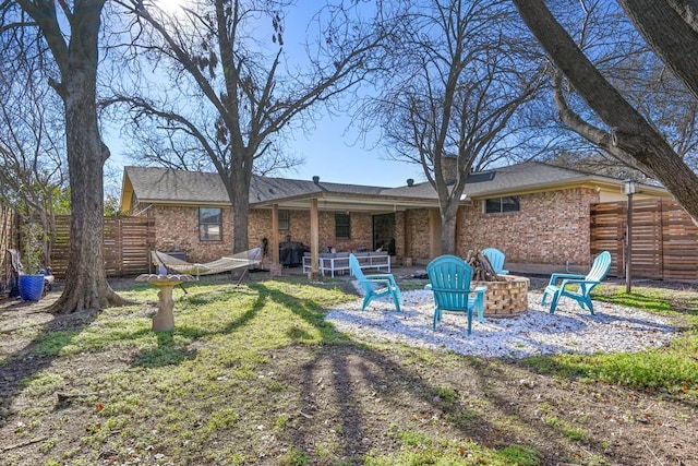 rear view of house with brick siding, fence, and a fire pit