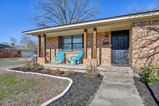 doorway to property featuring covered porch and brick siding