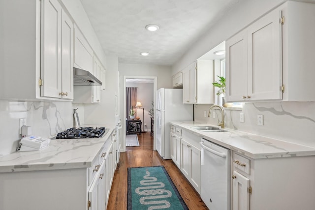 kitchen featuring white cabinets, a sink, wall chimney range hood, wood finished floors, and white appliances