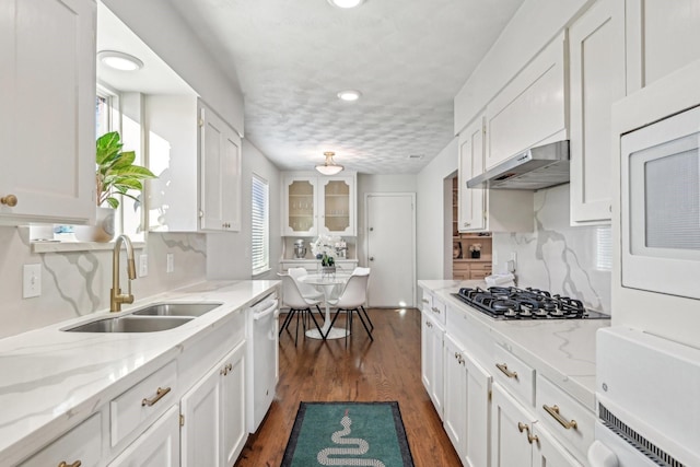 kitchen featuring white dishwasher, under cabinet range hood, a sink, gas stovetop, and white cabinets