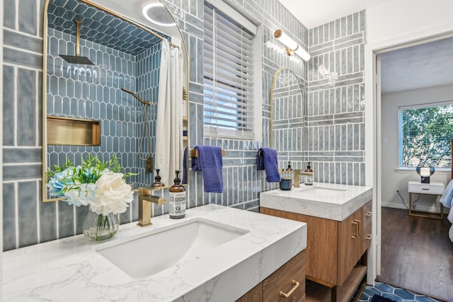 bathroom featuring two vanities, a sink, a tile shower, and wood finished floors