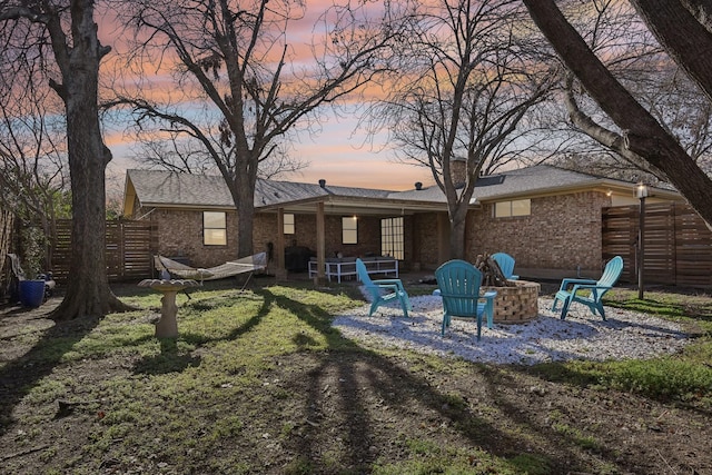 back of house at dusk featuring brick siding, fence, and a fire pit