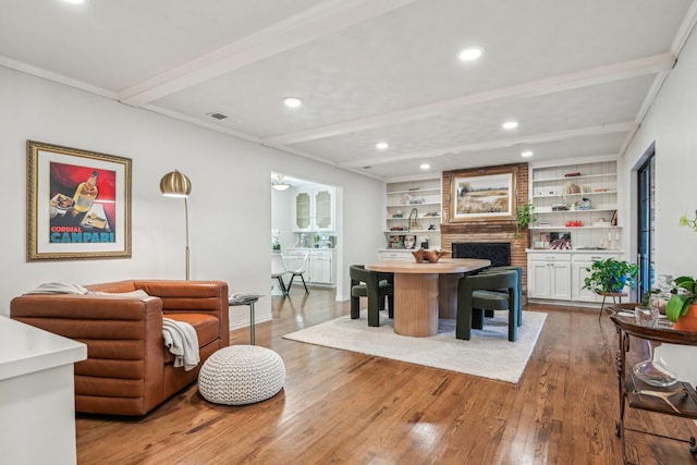 interior space with a fireplace, visible vents, built in features, light wood-style floors, and beamed ceiling