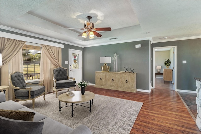 living room featuring dark wood-type flooring, a textured ceiling, a tray ceiling, crown molding, and ceiling fan