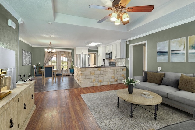 living area with a textured ceiling, ceiling fan with notable chandelier, dark wood-style floors, a tray ceiling, and crown molding