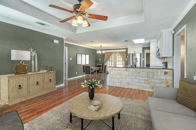 living room with a raised ceiling, ornamental molding, hardwood / wood-style flooring, a textured ceiling, and ceiling fan with notable chandelier