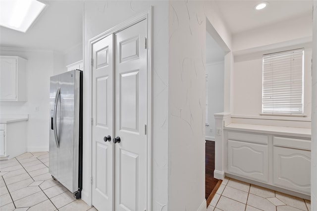 interior space featuring stainless steel fridge with ice dispenser, white cabinetry, light tile patterned flooring, and crown molding