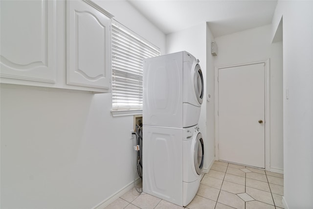 laundry area featuring stacked washer and dryer, cabinets, and light tile patterned floors