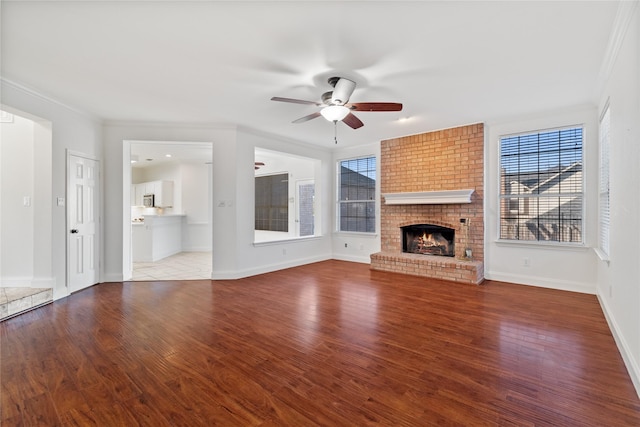 unfurnished living room featuring ceiling fan, a brick fireplace, crown molding, and hardwood / wood-style flooring