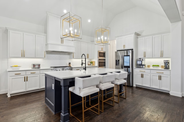 kitchen with an island with sink, appliances with stainless steel finishes, white cabinets, and decorative light fixtures