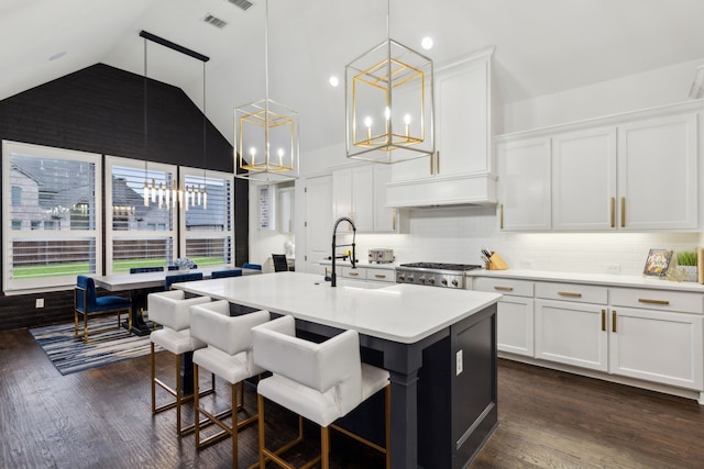 kitchen featuring lofted ceiling, sink, white cabinetry, decorative light fixtures, and a center island with sink