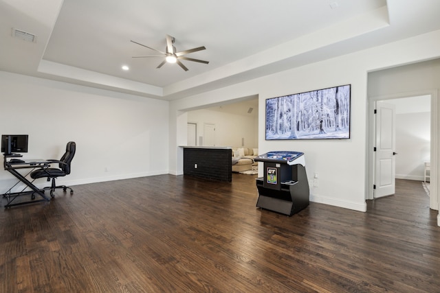 home office featuring a tray ceiling, dark wood-type flooring, and ceiling fan