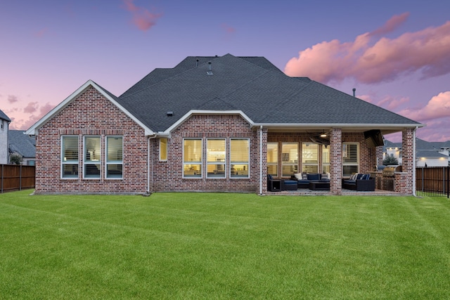 back house at dusk with an outdoor living space, a lawn, ceiling fan, and a patio area