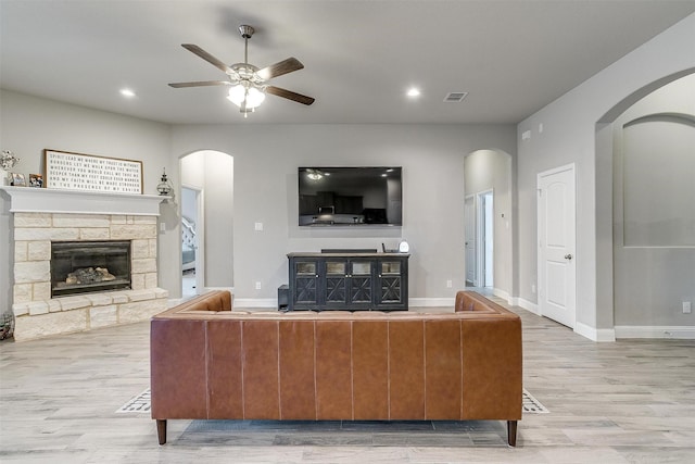 living room featuring hardwood / wood-style floors, ceiling fan, and a stone fireplace