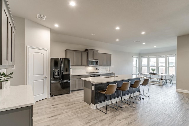 kitchen with stainless steel appliances, sink, light wood-type flooring, an island with sink, and a breakfast bar