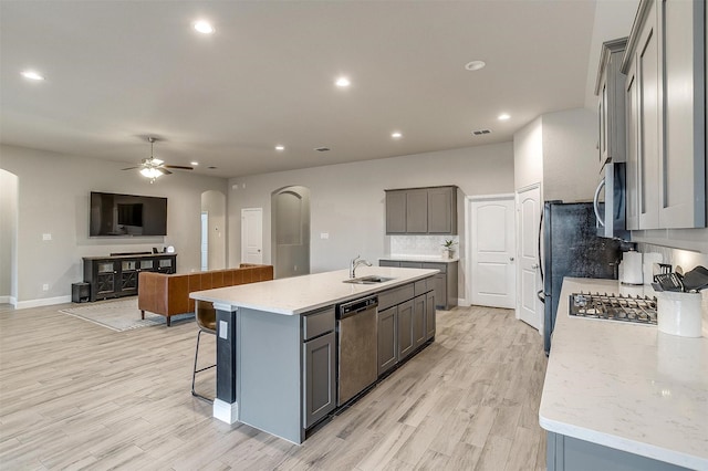 kitchen with stainless steel appliances, sink, gray cabinets, and an island with sink