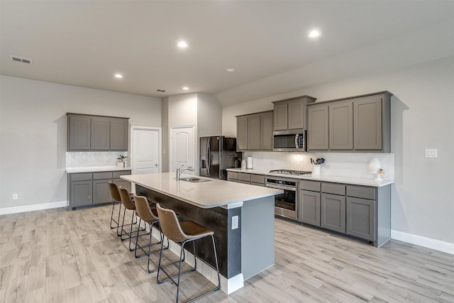 kitchen featuring appliances with stainless steel finishes, a kitchen bar, gray cabinets, and a center island with sink