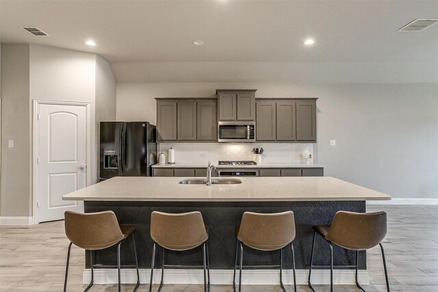 kitchen featuring a kitchen breakfast bar, a kitchen island with sink, gray cabinets, and appliances with stainless steel finishes