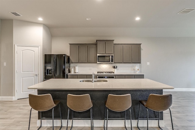 kitchen featuring sink, gray cabinets, stainless steel appliances, a kitchen island with sink, and decorative backsplash