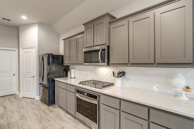 kitchen with gray cabinetry, stainless steel appliances, light stone counters, and tasteful backsplash